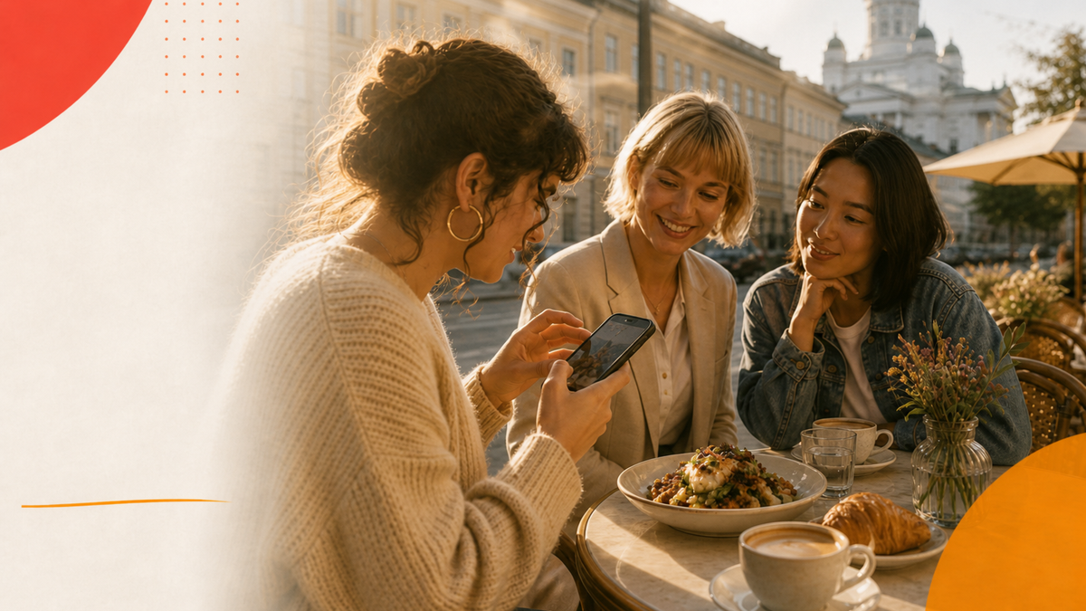 Two people talking at a neighbourhood café table while looking at a phone, illustrating peer-level trust in small creator recommendations